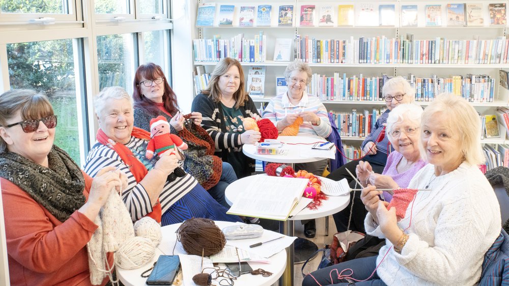 Eight ladies sitting around a table knitting and crocheting.