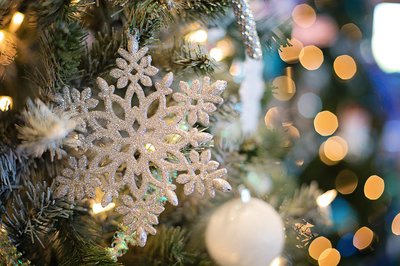 A close-up image of a Christmas tree with a white snowflake ornament at the front