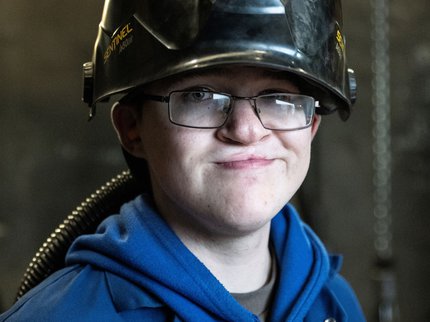 An Inspire College learner wearing a protective visor and branded work uniform in an engineering workshop.