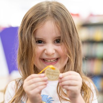 Girl smiling holding medal for reading in the library