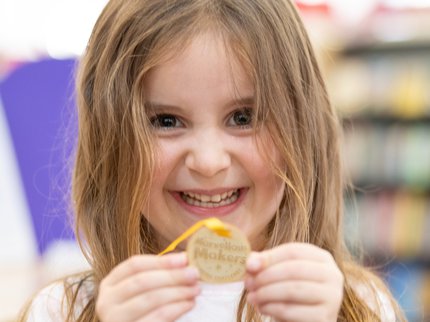 A smiling girl holds up her Summer Reading Challenge Medal