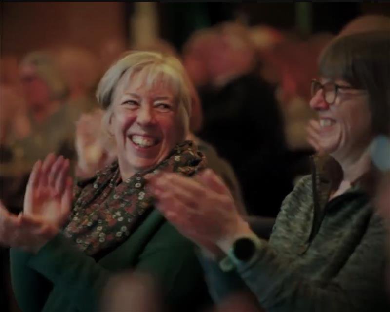 Two ladies in an audience clapping and laughing.