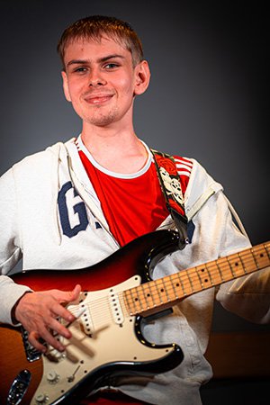 Male AO Pioneer, Marshall smiling and playing an electric guitar